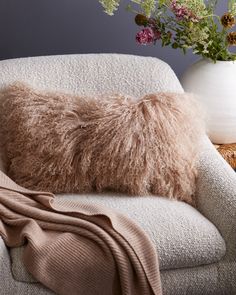 a fluffy pillow on a chair next to a vase with flowers