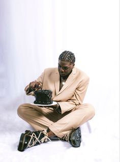 a man sitting on the ground with a cake in his hand and wearing a suit