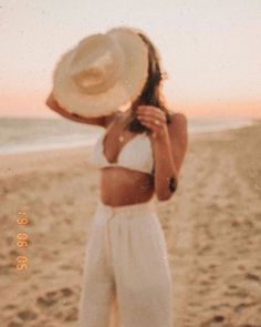 a woman standing on top of a beach next to the ocean wearing a white hat