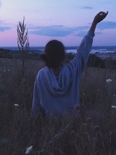 a woman is sitting in the grass with her arms up and looking at the sky