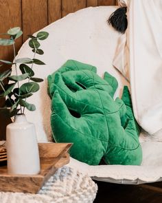 a green pillow sitting on top of a white chair next to a potted plant