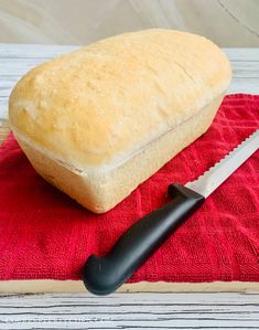 a loaf of bread sitting on top of a red towel next to a knife