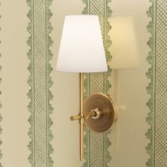 a wall lamp with a white shade on it's side next to a green striped wallpaper