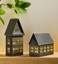 two small black houses sitting next to each other on a wooden shelf near a potted plant