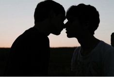 two people standing next to each other with the sun setting in the sky behind them