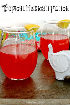 two glasses filled with liquid sitting on top of a table next to some lemon wedges