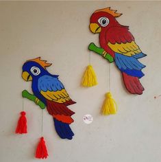 two colorful parrots are hanging on the wall with tassels attached to them