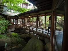 a woman standing on a bridge over a stream in a japanese style house with trees and rocks