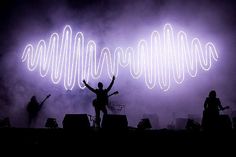 two people standing on stage with their arms up in the air and lights behind them