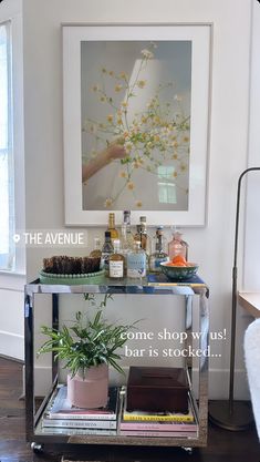 a bar cart with drinks and plants on it in front of a window that reads the avenue