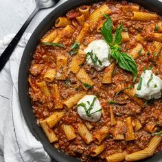 a skillet filled with pasta and sauce on top of a white cloth next to utensils