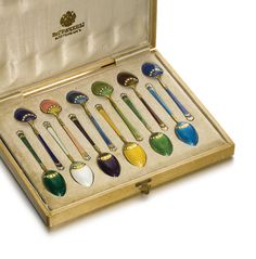 a set of seven spoons in a box with gold trimming and colored handles