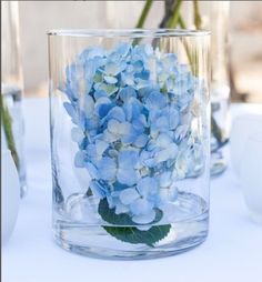 there is a vase with blue flowers in it on top of a white table cloth