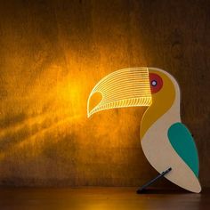 a colorful bird shaped lamp sitting on top of a wooden table next to a wall