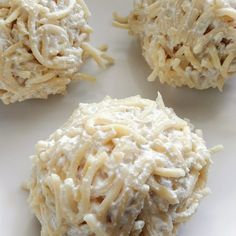 four balls of food sitting on top of a white plate with noodle toppings