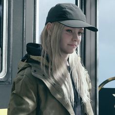 a woman with long blonde hair wearing a hat and jacket on a bus looking out the window