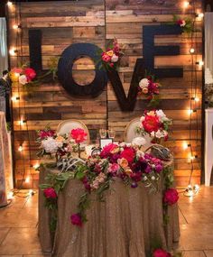 a table with flowers and lights on it in front of a wooden sign that says love