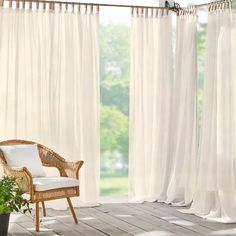 a wicker chair sitting in front of a window with white drapes on it