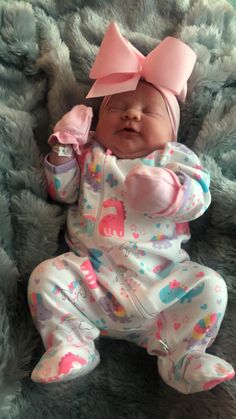 a baby laying on top of a blue blanket wearing a pink bow and holding a cup