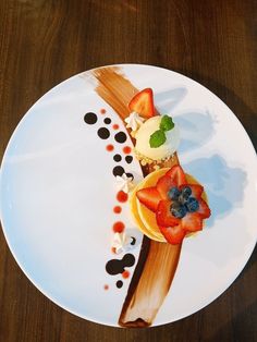 a white plate topped with fruit and pastry on top of a wooden table next to a knife