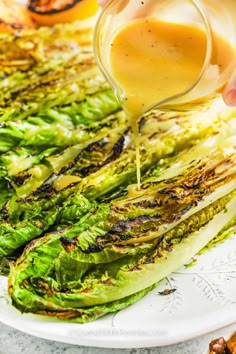 someone pouring dressing on top of grilled lettuce in a white plate with other vegetables