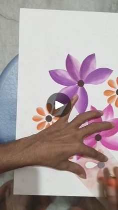 a person's hand holding onto a painting with flowers painted on the paper next to it