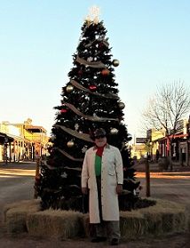 a man standing next to a christmas tree in the middle of a street with other buildings