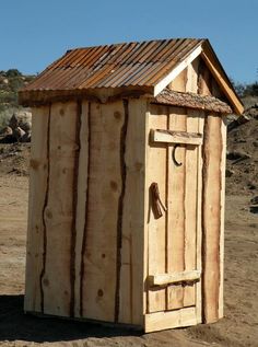 a small wooden outhouse sitting on top of a dirt field