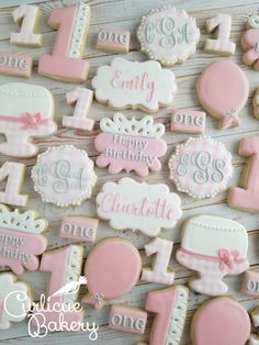 decorated cookies with pink and white icing are arranged on a wooden board for a first birthday party