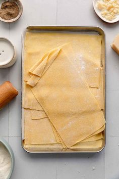 a pan filled with uncooked pasta next to bowls of flour and other ingredients