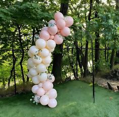 a bunch of balloons are attached to a pole in the grass with trees behind it