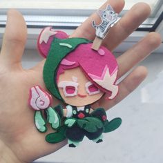 a hand holding a small doll with pink hair and green clothes on it's fingers