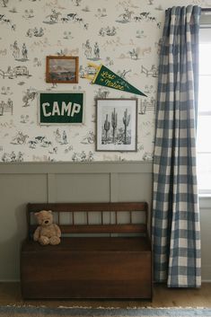 a teddy bear sitting on top of a wooden bench in front of a wall with pictures