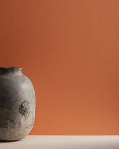 a gray vase sitting on top of a white table next to an orange painted wall