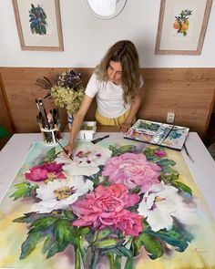 a woman sitting at a table painting flowers