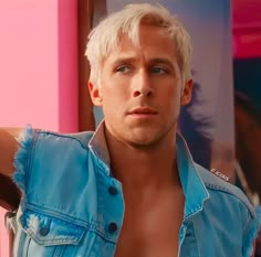 a man with white hair wearing a blue jean jacket and posing for a photo in front of a pink wall