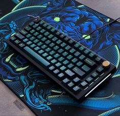 a computer keyboard sitting on top of a blue and green dragon print mouse pad,