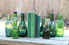 several green glass bottles sitting on top of a wooden table next to books and magazines