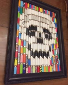 an art piece made out of crayons on a wooden table with a black frame