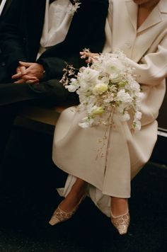 a man and woman sitting next to each other on a bench with flowers in their hands