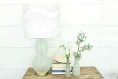 two vases and a lamp sitting on a table next to each other in front of a white wall