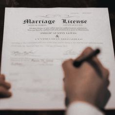 a person writing on a marriage license document with a pen and paper in front of them