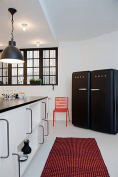 a kitchen with two black refrigerators and a red rug in front of the counter