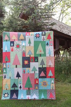 a patchwork quilt hanging on the side of a tree in front of a house