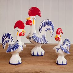 three ceramic rooster figurines sitting on top of a wooden table