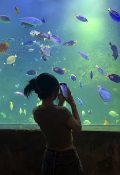 a woman taking a photo of an aquarium with her cell phone while looking at the fish