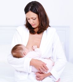 a woman holding a baby wrapped in a white bathrobe while sitting on a bed