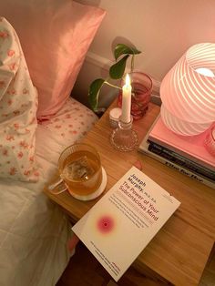 a table with a book and candle on top of it next to a glass cup