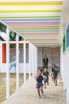 children are running down the sidewalk under a colorful awning over an area with white pillars