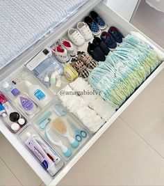 an open drawer filled with baby items on top of a white floor next to a bed